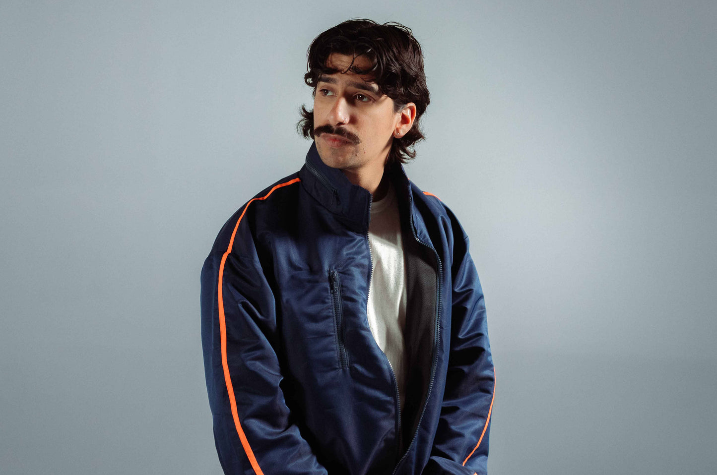 STMNT Wear deep navy track jacket with orange accent stripe over white tee, studio portrait with high collar