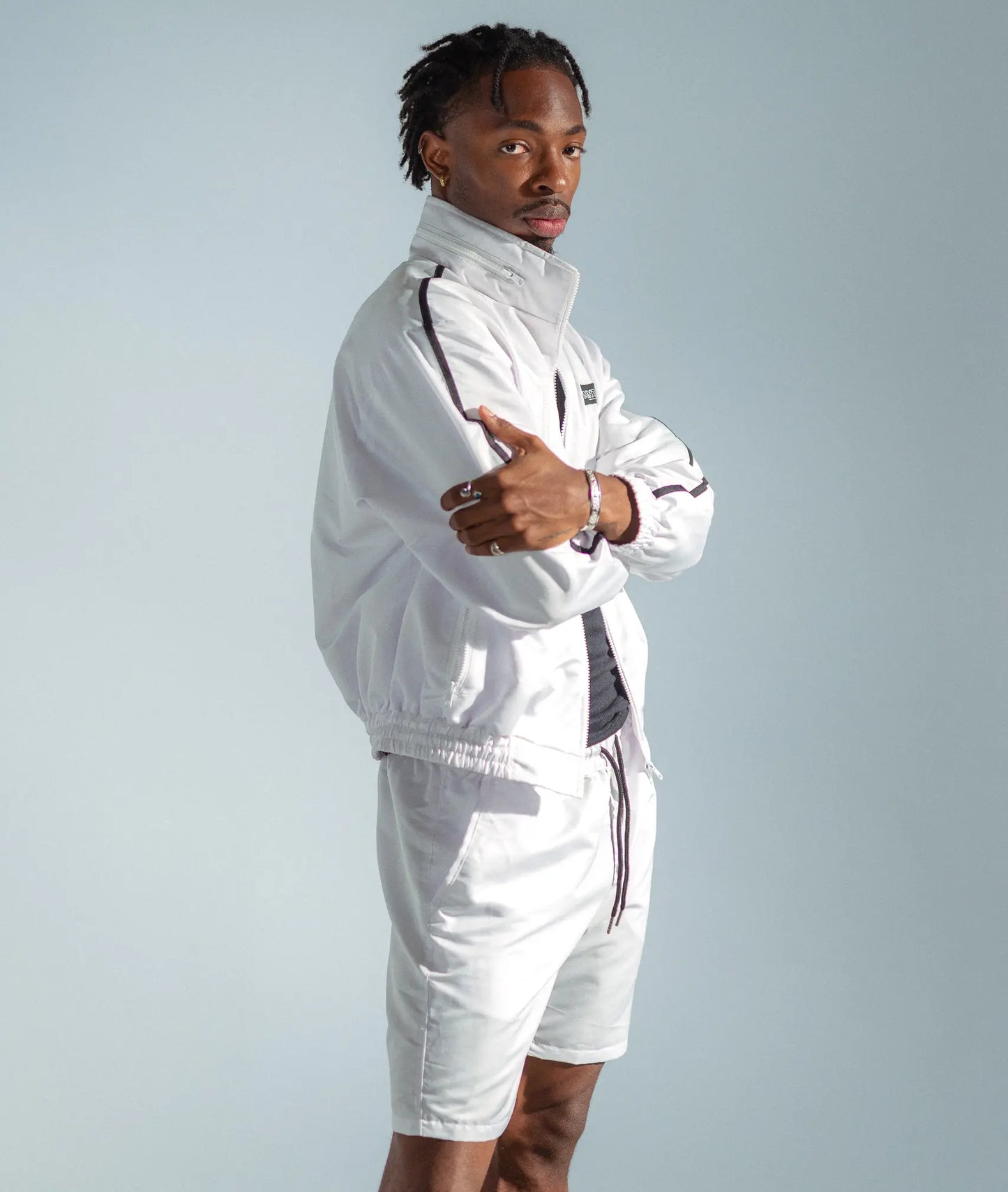 STMNT Wear white track jacket with black stripe, side profile with arms crossed showing logo and trim