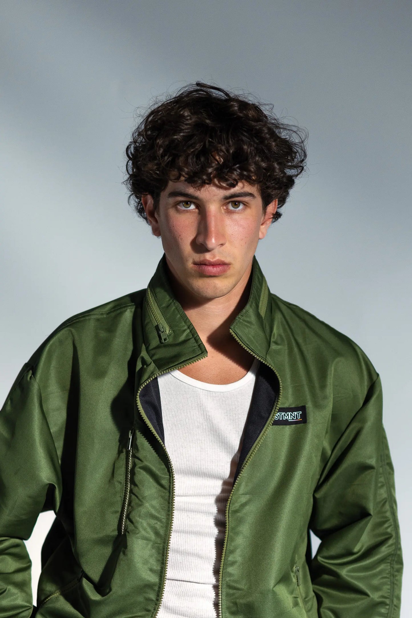 STMNT Wear Green Full Tracksuit - olive track jacket with STMNT chest logo over white tee, portrait closeup studio shot