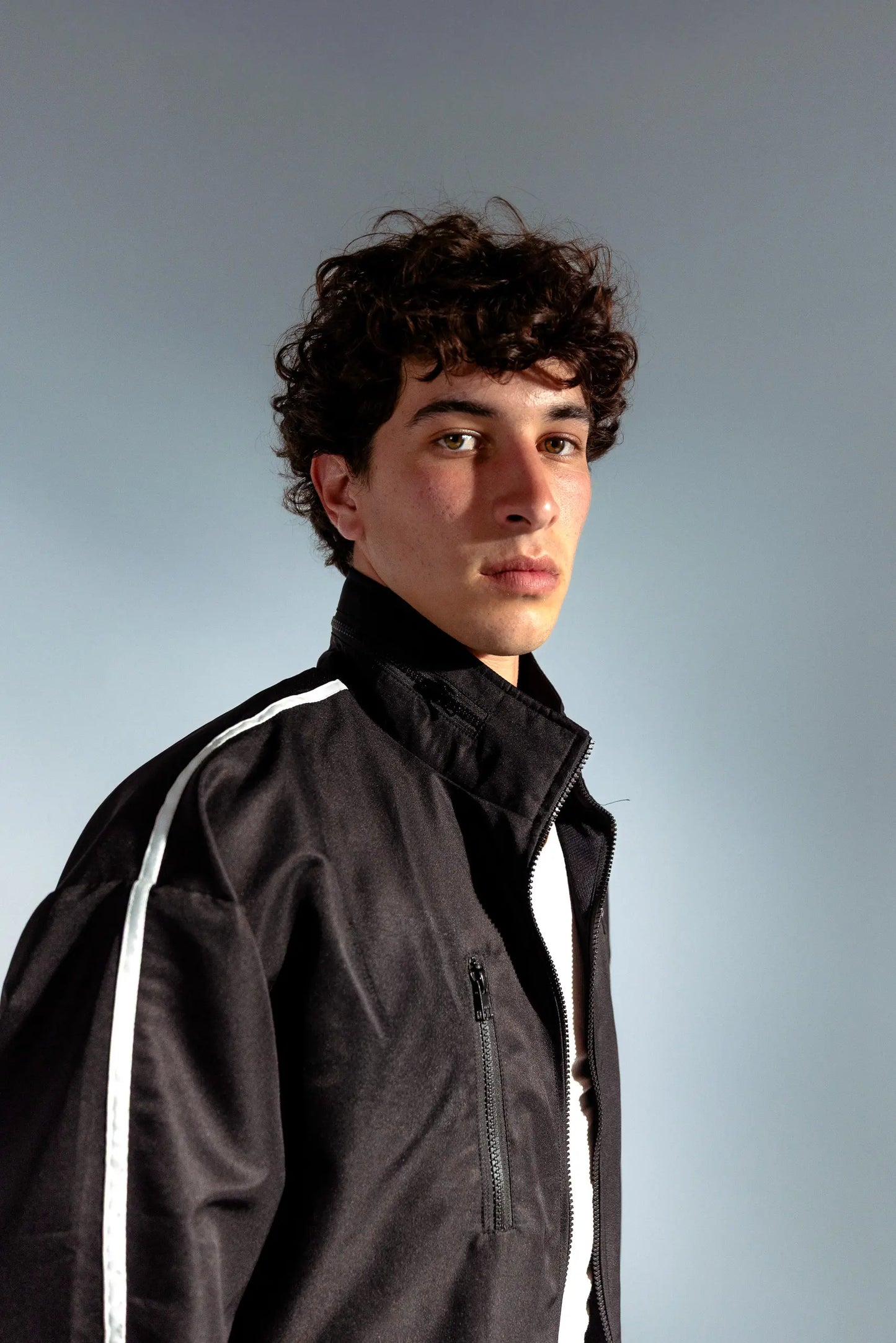 STMNT Wear black track jacket portrait, model looking over shoulder showing collar and stripe detail
