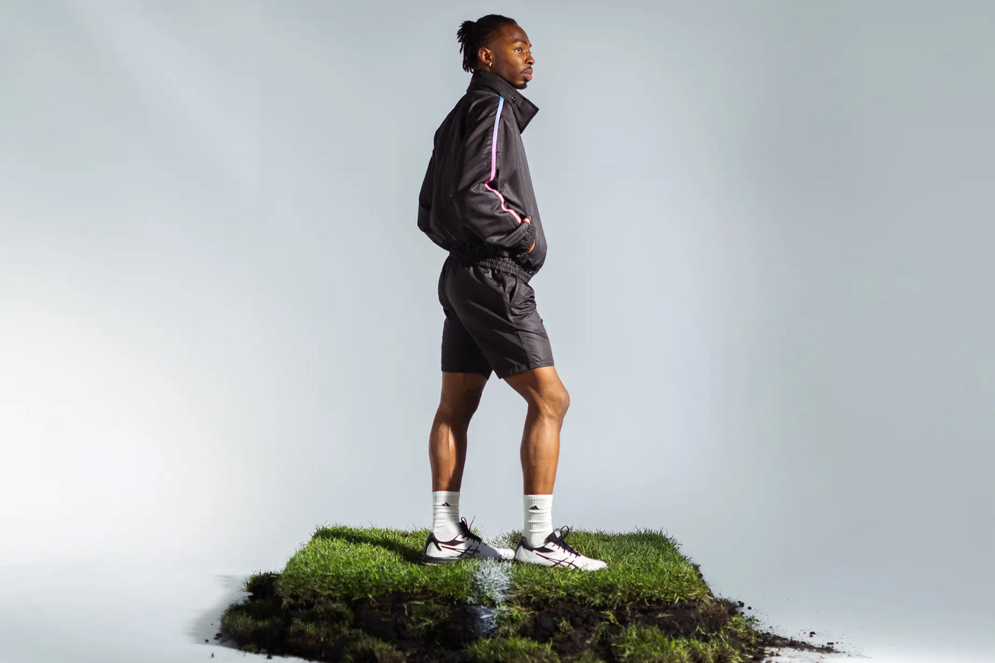 Model wearing STMNT Wear First Edition black athletic shorts and jacket standing on soccer pitch turf