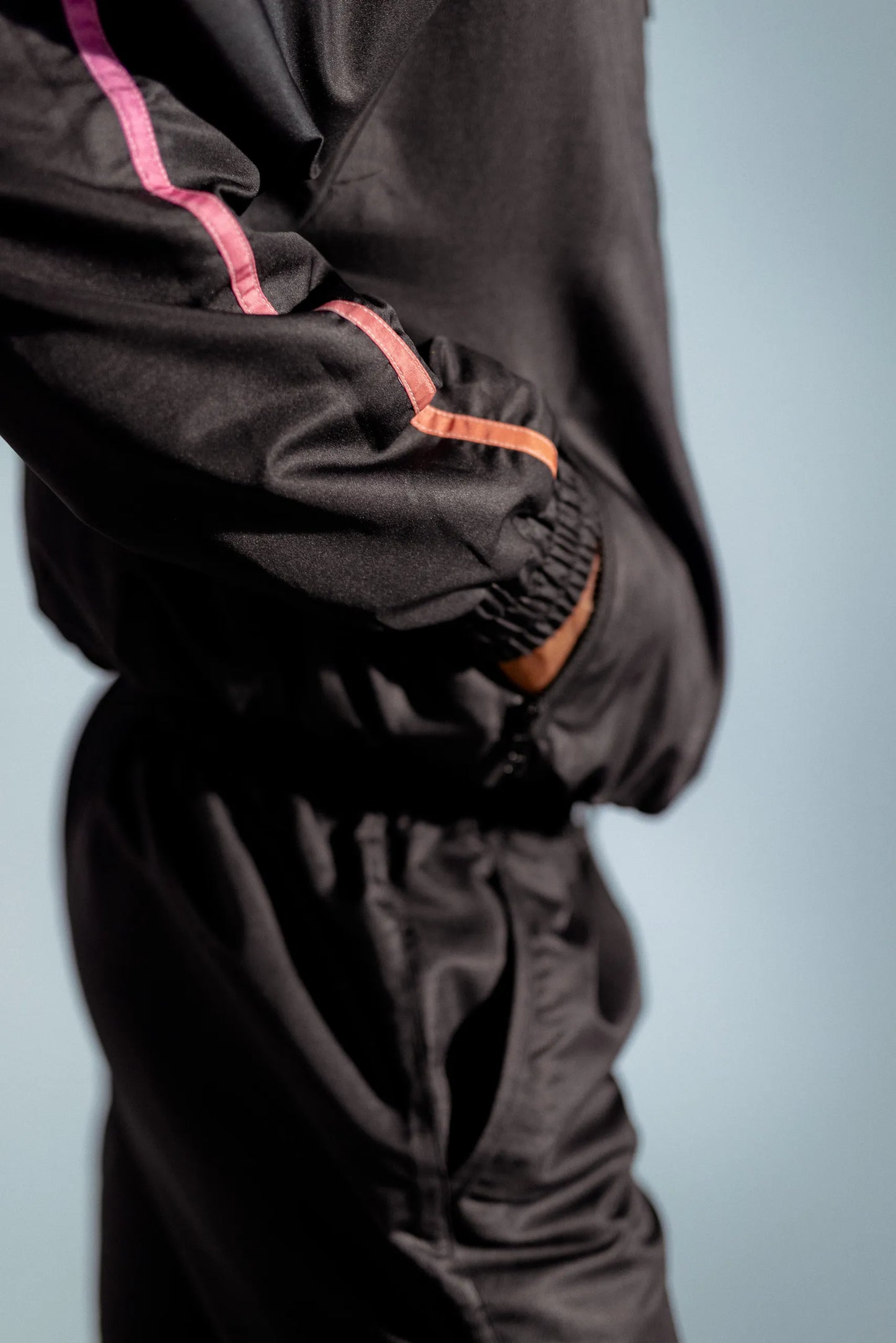 Side detail of STMNT Wear First Edition black jacket showing pink gradient stripe trim and zip pocket on sleeve