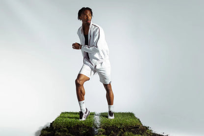 Model in motion wearing STMNT Wear white athletic shorts and track jacket on soccer pitch turf cut-out in a studio