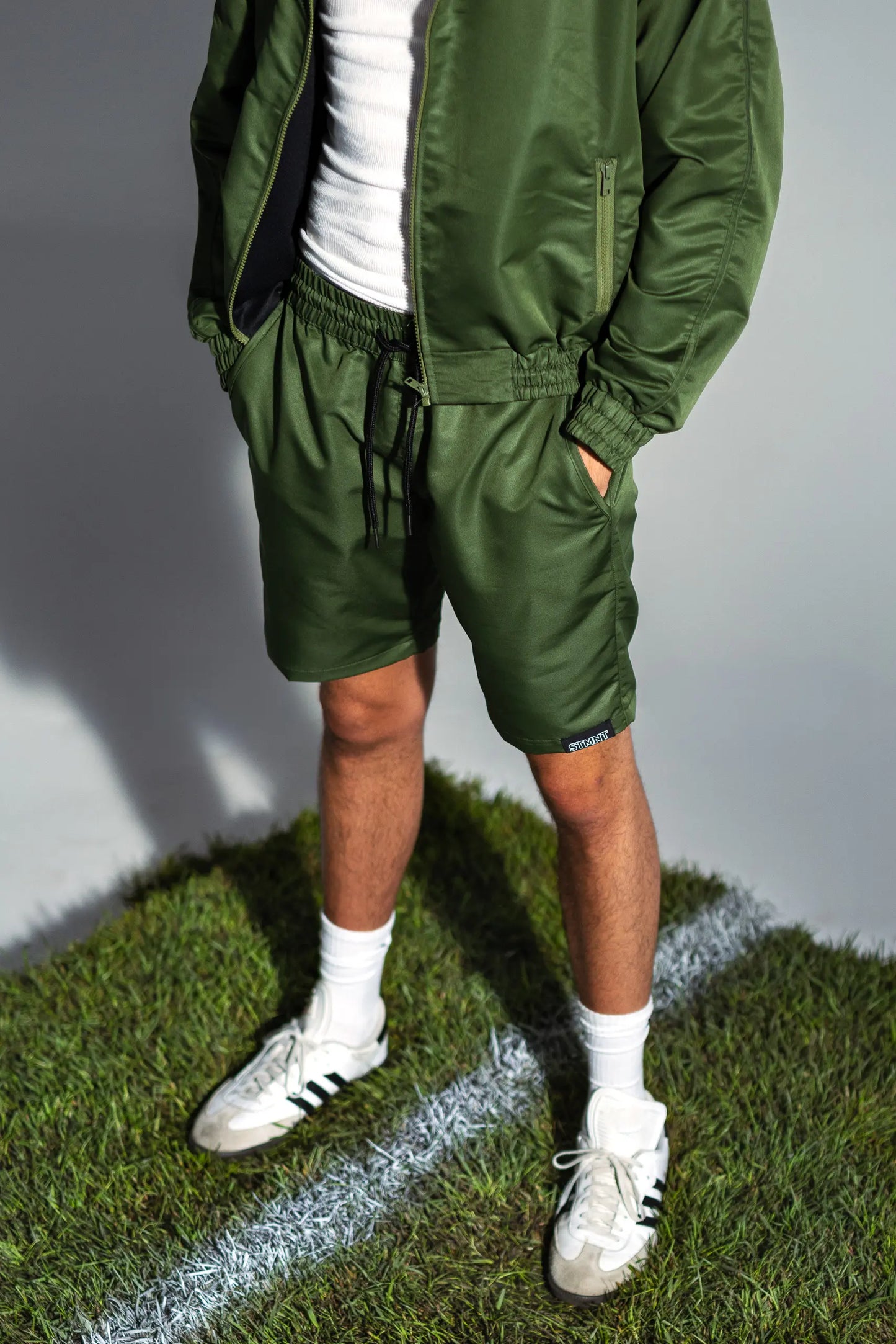 STMNT Wear green drawstring shorts and matching jacket lower body view on soccer pitch grass cut-out in a studio