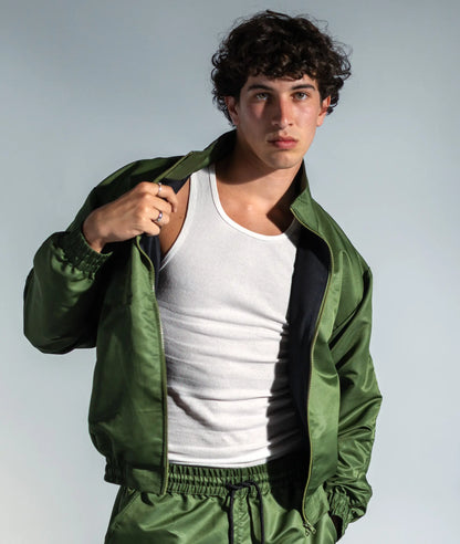 STMNT Wear olive green track jacket open over white tank top, front view showing relaxed athletic fit