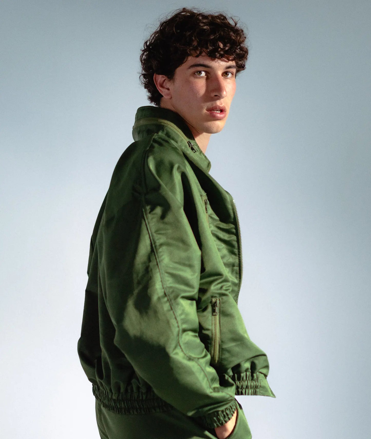STMNT Wear olive green track jacket side profile, model looking back with hands in pockets