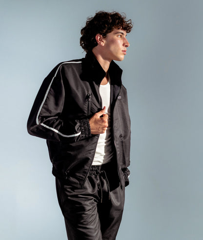 Model in STMNT Wear Black Full Kit - open track jacket over white tee with matching shorts, side profile studio shot