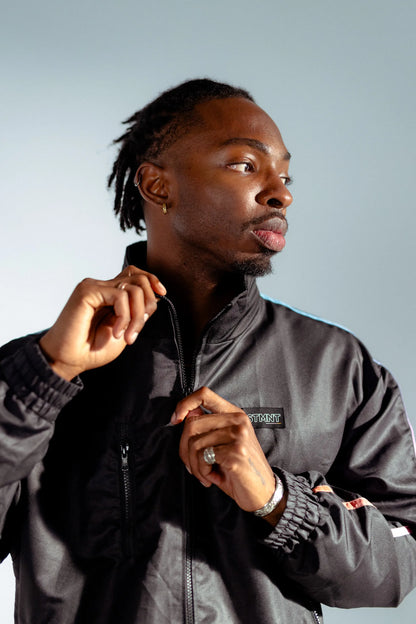 Model zipping STMNT Wear First Edition black track jacket with gradient stripe, portrait with high collar up
