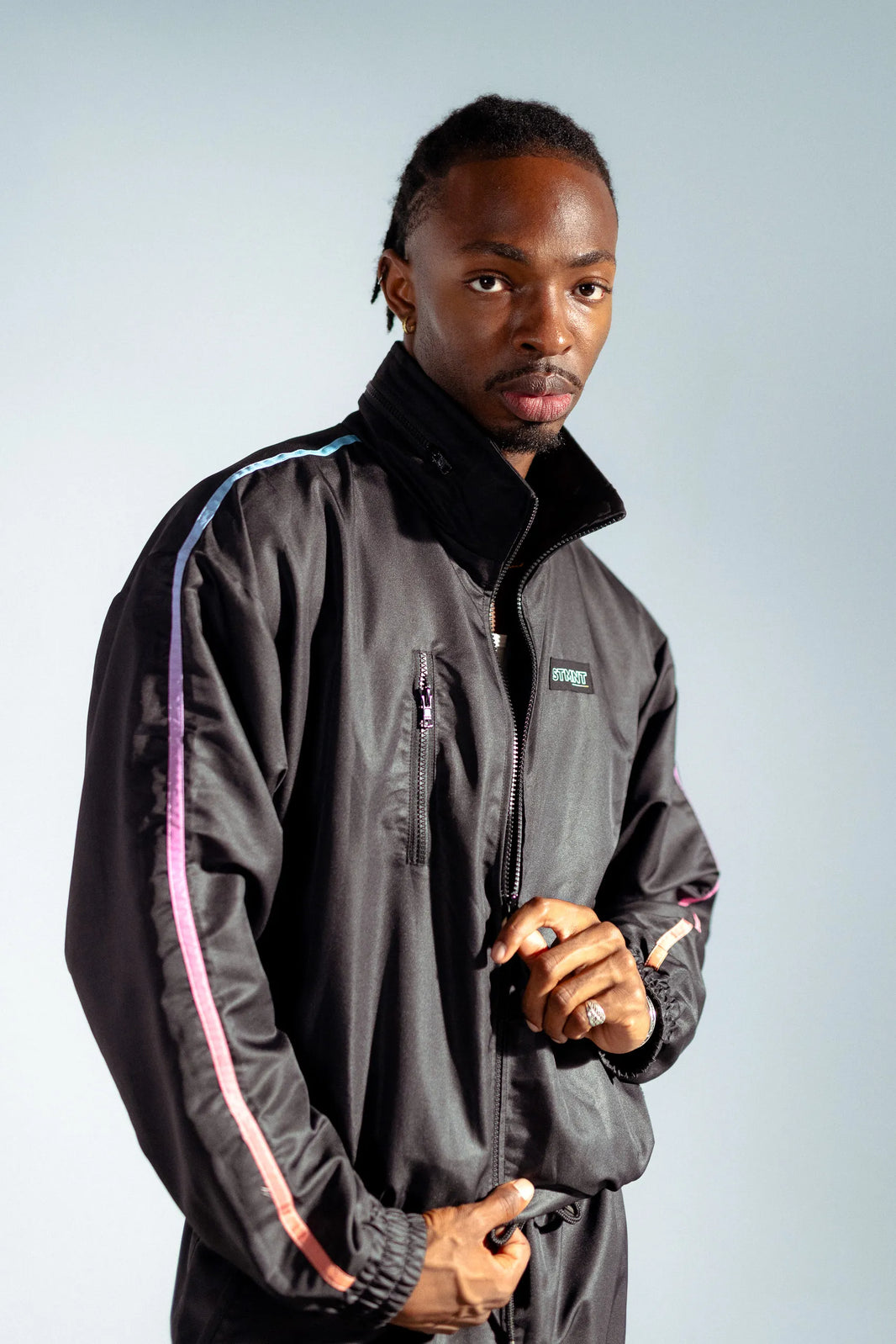 STMNT Wear First Edition black track jacket front view showing gradient rainbow sleeve stripe and STMNT logo patch