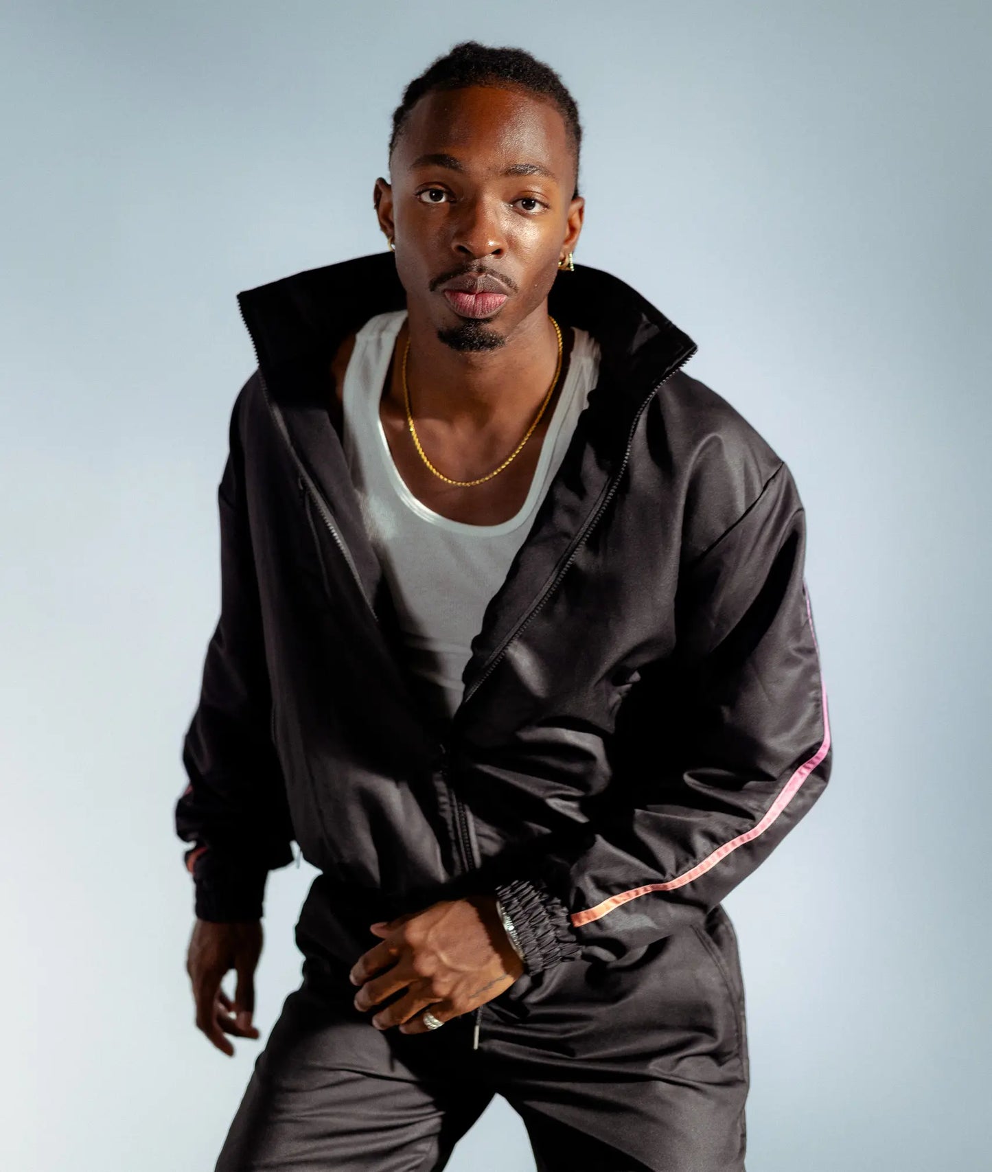 Model leaning forward in STMNT Wear First Edition black track jacket with pink-blue gradient accent stripes, dynamic street pose