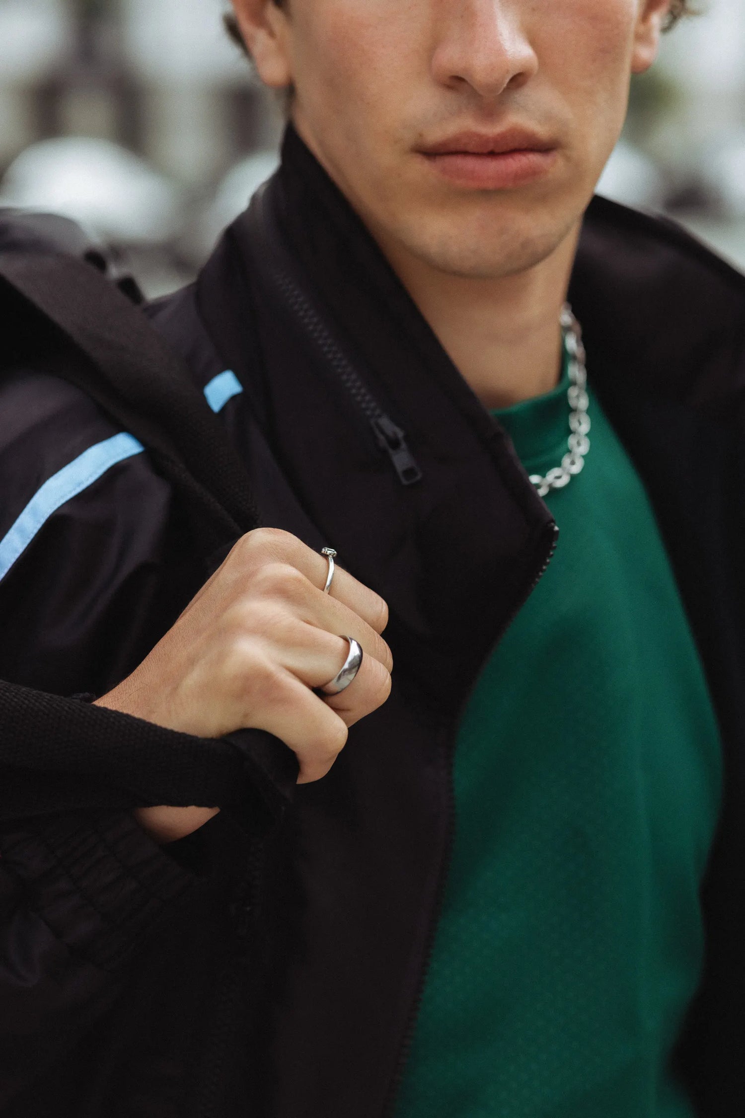 Close-up of STMNT Wear First Edition black track jacket with blue stripe detail over green tee - streetwear outfit detail