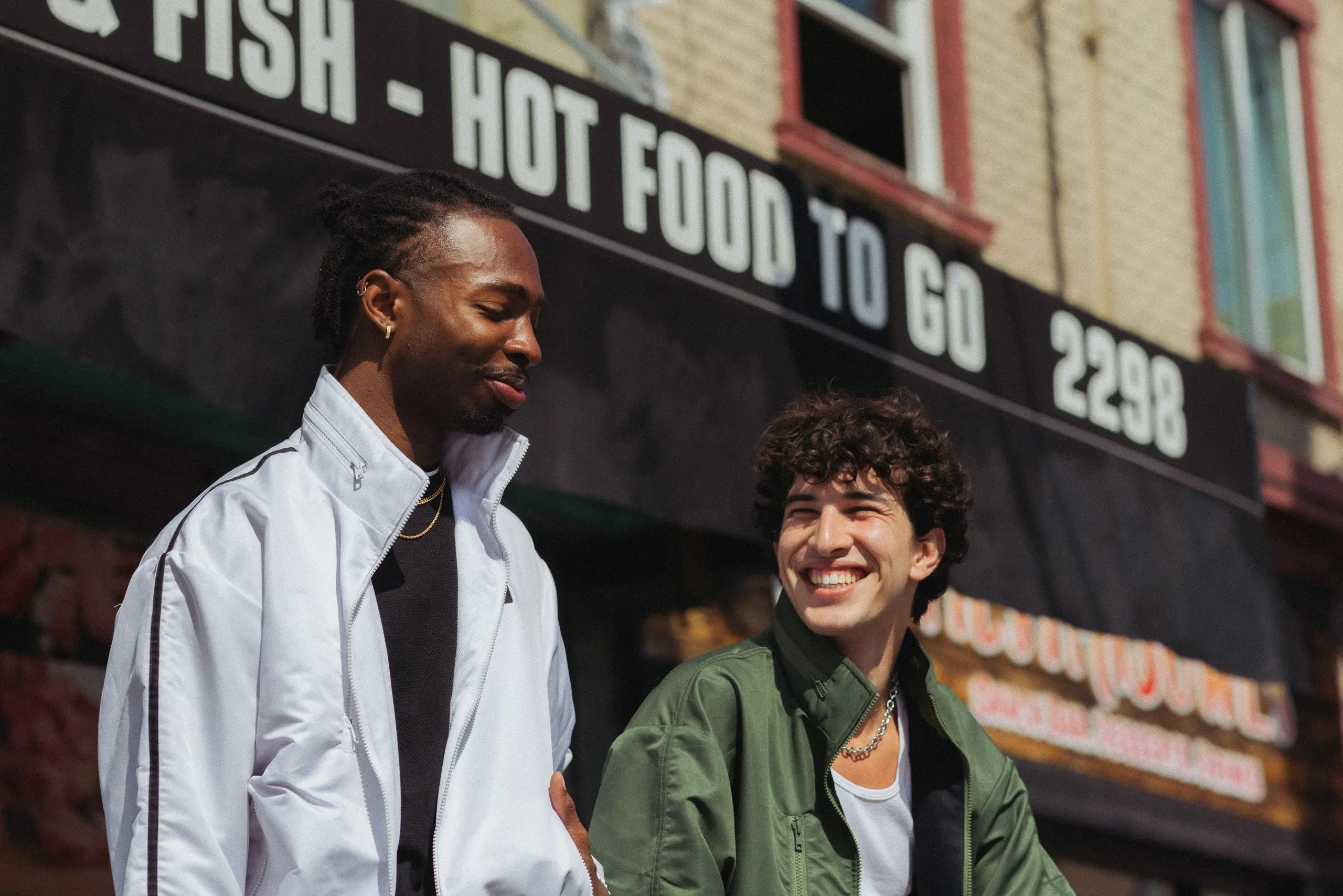 Two models in STMNT Wear track jackets laughing together on a sunny city street - athletic streetwear lifestyle